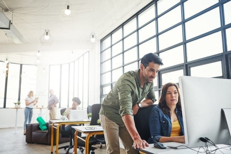 Shot of a man assisting his colleague at her desk in office with green blocks in background